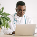 A doctor working at a laptop in an office.