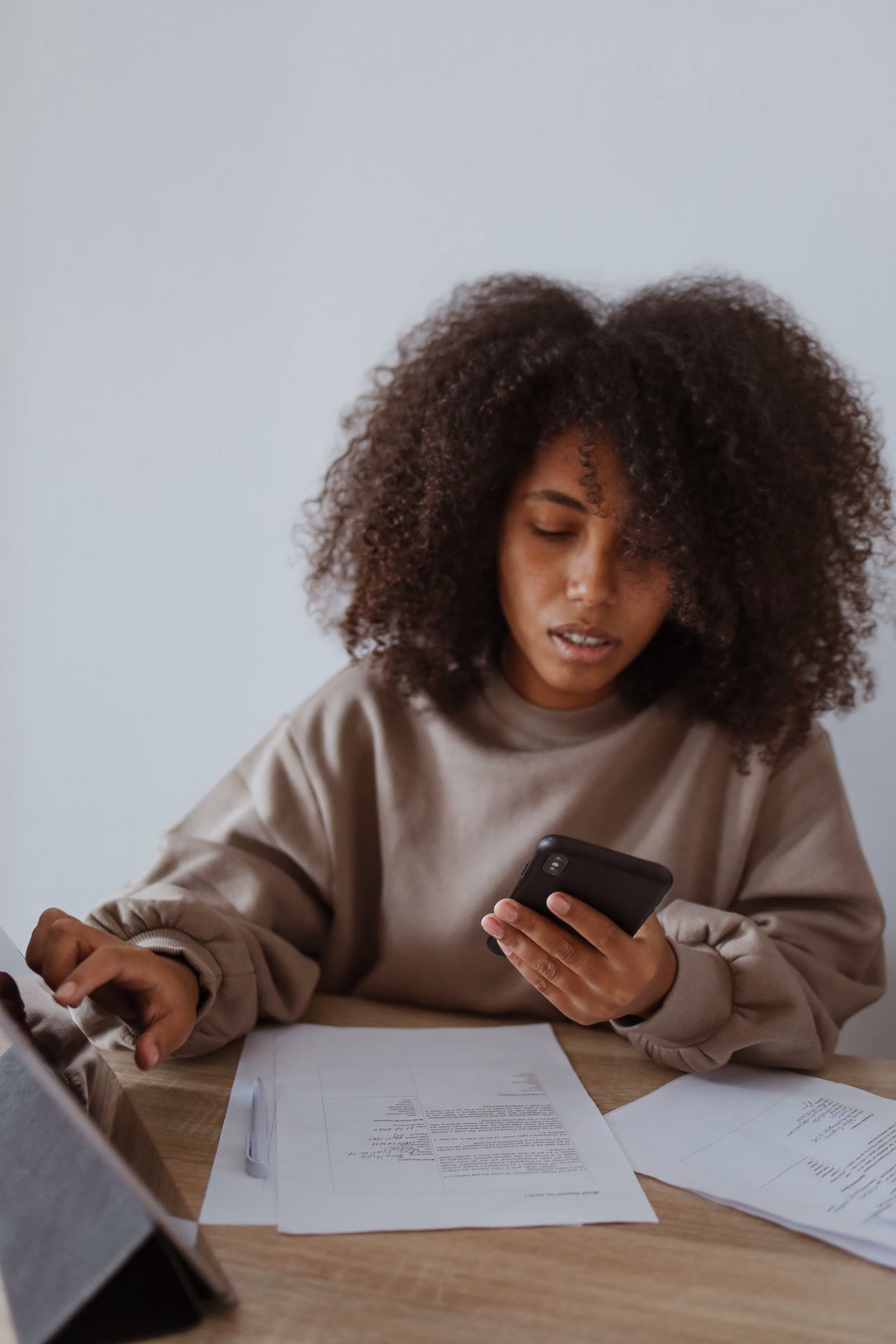 A woman using a smartphone while working with documents.