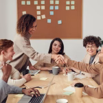 Team members discussing work and shaking hands around a meeting table.