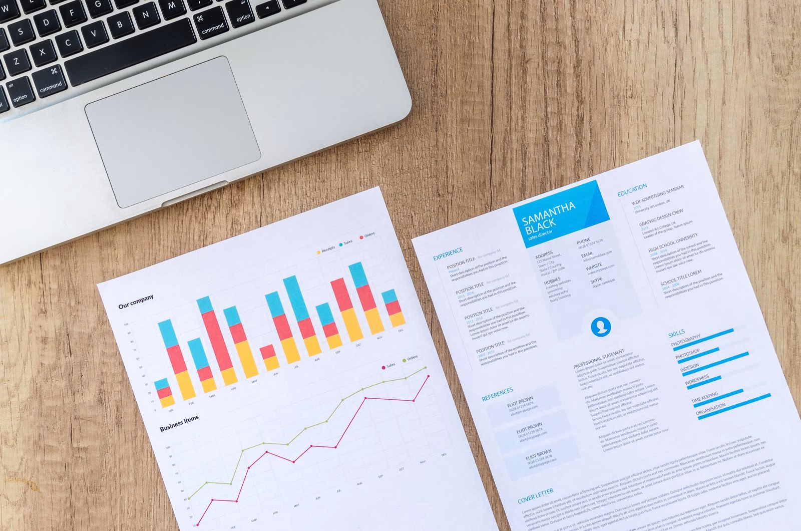 Printed business documents beside a laptop on a wooden desk.
