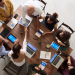 An office team discussing documents and laptops around a large table.